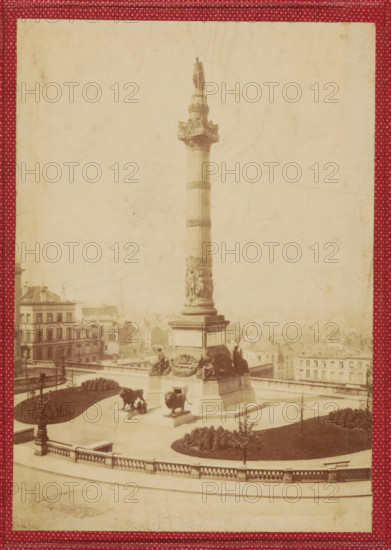 View of the Congress Column in Brussels, photograph, page, Brussels, c. 1854 - in or before 1859, photographer, paper, albumen print, height 155 mm x width 109 mm, Photo on front cover, column, pillar, architecture, Congress column, A tall stone column topped by a standing statue rises from a square base adorned with sculpted figures, with two large lion statues positioned on pedestals near the base; the column and base are set within a paved terrace bordered by a balustrade and low curved walls, with manicured lawns and planted beds visible in the surrounding area; several multi-story buildings with rows of windows and pitched roofs are visible in the background; a few people are seen near the monument and on the terrace; the image has a faded, sepia tone and is framed by a patterned red border.