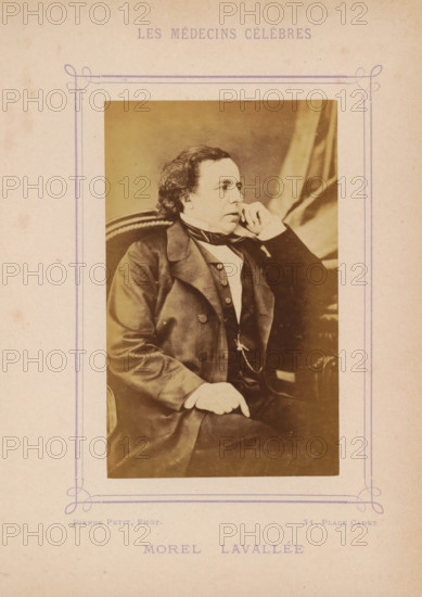 Portrait of Victor-Auguste-François Morel-Lavallée, Morel Lavallée, photograph, page, inscription: 'Publication de la Revue de literature médicale, du, DF Bremond, 20, Passage Saulnier, Paris) - No.', photographer: Pierre Petit, c. 1871 - c. 1879, paper, albumen print, height 90 mm x width 56 mm, Person, Victor Morel-Lavallée, historical persons, adult man, A sepia-toned portrait of a seated man in formal attire within a decorative bordered frame; he has wavy dark hair and is posed in profile with his head turned to the side, resting his cheek on one hand while the other hand rests on his knee; he wears a dark coat over a buttoned waistcoat and a white shirt with a neckcloth, and a watch chain is visible across his waist; the chair behind him has a rounded back with a visible edge, and draped fabric appears in the background; the image is set on aged paper with a faint ornamental border around the photograph.
