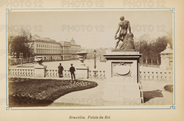 View of the Royal Palace in Brussels, Bruxelles. Palais du Roi, photograph, page, Brussels, c. 1875 - c. 1880, photographer, paper, albumen print, height 101 mm x width 175 mm, monument, statue, palace, Koninklijk Paleis (Brussel), A sepia-toned photograph showing a formal exterior scene with a large stone balustrade and decorative urns, a paved walkway curving past a planted lawn, and two men in dark coats and hats standing near the railing facing away from the camera; a tall stone pedestal topped with a muscular nude male statue seen from behind stands prominently to the right, draped fabric carved beside the figure, and an ornate rectangular panel on the pedestal; behind the balustrade a wide open paved forecourt stretches toward a long classical building with rows of windows and columned portico, trees and garden elements are visible at the edges of the scene, and a freestanding lamppost stands near the center distance.