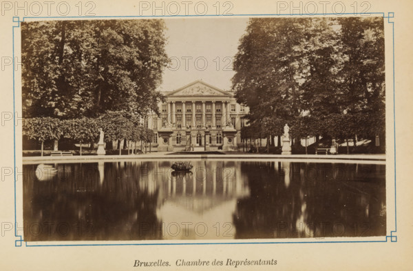 View of the Palace of the Nation in Brussels, Bruxelles. Chamber of Representatives, photograph, page, Brussels, c. 1875 - c. 1880, photographer, paper, albumen print, height 103 mm x width 171 mm, palace, garden pond, Palace of the Nation, A sepia-toned photograph shows a neoclassical building with a triangular pediment and a row of tall columns across its facade, flanked by trees on both sides; in front of the building there is a rectangular reflecting pool with a small circular planted feature in its center and statues on pedestals along the pool edge, and the building and trees are mirrored in the pool’s calm surface.