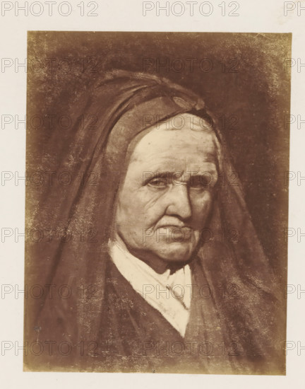 Photo reproduction of a portrait of Marie de Médicis by Paul Delaroche, photograph, reproduction, page, after painting by Paul Delaroche, c. 1858 - c. 1863, photographer, paper, albumen print, height 142 mm x width 110 mm, Person, Maria de' Medici, picture, painting, old woman, A sepia-toned portrait of an elderly person wearing a dark hooded garment and a light-colored scarf, showing a face with deep wrinkles, downturned mouth, and heavy eyelids. The hood frames the head and casts shadows across the forehead and cheeks. The background is dark and textured, and the image is bordered by a lighter margin. The clothing appears layered with visible folds and a contrast between the dark outer garment and the lighter fabric at the neck.