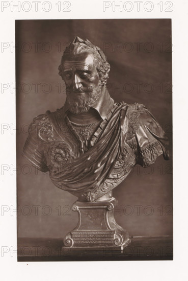 Bust of Henry IV of France, displayed during the Exposition Rétrospective of 1873 in Tours, France, page, photomechanical print, maker: Gabriel Blaise, Tours, 1873, paper, Woodburytype, Woodburytypie, height 195 mm x width 126 mm, Person, Henry IV (King of France and Navarre), piece of sculpture, reproduction of a piece of sculpture, temporary exhibition, 'Salon', Period, 1873-05-03 - 1873-05-25, A monochrome photograph of a sculpted bust showing a bearded man with curly hair and a laurel-like headpiece, wearing ornate armor and a draped cloak; the bust rests on a decorative pedestal with carved scroll details and a rectangular base, and the background is plain and darker than the sculpture.