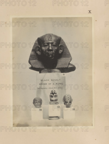 Four Egyptian objects, including a fragment of a sculpture, the head of a pharaoh and a sculpture of a seated scribe, photograph, page, number: 'XII', c. 1890 - c. 1895, photographer, paper, gelatin silver print, developed gelatin silver print, height 213 mm x width 157 mm, sculpture, king, writer, poet, author, A photograph shows a dark sculpted head wearing a striped headpiece with flared sides and a smooth face with prominent ears, positioned above three smaller sculpted heads on pedestals; the central smaller sculpture is a seated figure on a stepped base, flanked by a rough-textured head on the left and a head with a patterned headdress on the right, all set against a pale background and framed by a lighter rectangular border within a larger mottled sheet.