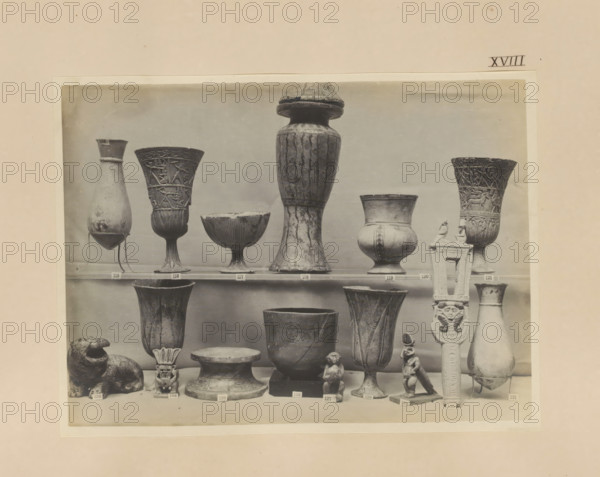 Sixteen Egyptian objects, vases, a sculpture of Bes and a sistrum, photograph, page, number: 'XVIII', c. 1890 - c. 1895, photographer, paper, gelatin silver print, developing gelatin silver print, height 158 mm x width 213 mm, sculpture, containers, representations, Egyptian gods, demi-gods, heroes, etc. (BES), A black and white photograph of a display of various ancient-style vessels and small sculptures arranged on shelves, including tall fluted goblets with carved figures, bulbous jars with narrow necks, shallow bowls on stems, a large tall vase with a rounded lid, a carved column-like object with decorative figures, a seated animal sculpture, small human or animal figurines, and several pedestal bases, all shown against a plain background.