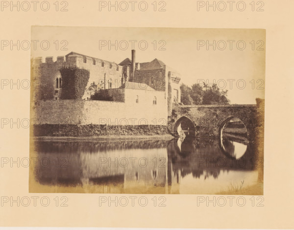 Gatehouse and bridge of Leeds Castle, photograph, page, inscription: 'No.4.', photographer: John Cruttenden, Leeds Castle, c. 1864 - in or before 1869, Leeds, paper, albumen print, height 144 mm x width 201 mm, landscape with tower or castle, castle, gate, entrance, A sepia-toned photograph of a stone building complex with crenellated walls and arched windows beside a bridge with two large stone arches spanning a calm body of water that reflects the arches and parts of the structure, with ivy growing on a section of the wall and trees visible behind the building.