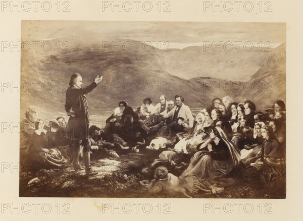 Photo reproduction of Sabbath in the Glen by Sir George Harvey, photograph, reproduction, page, photographer: Thomas Annan, after painting by George Harvey (Sir), c. 1865 - in or before c. 1870, paper, albumen print, height 146 mm x width 220 mm, meeting, assembly - AA - in the open air, Sabbath, Jewish religion, Scotland, A wide sepia-toned scene shows a standing man in dark clothing with one arm raised and a small book at his side facing a large seated and reclining crowd; the crowd includes men, women, and children in period-style clothing with shawls, bonnets, and coats, several people looking toward the standing man while others look outward or downward, and a few individuals appear to be resting or asleep; the foreground features rocks, grass, and a reclining figure facing away from the viewer, and a few animals lying on the ground; the background displays rolling hills and a cloudy sky.
