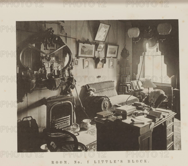 Interior of Room One in Little's Block of Harvard University, Room, no. 1 Little's Block, page, photomechanical print, c. 1870 - in or before 1875, paper, collotype, photoprint, height 165 mm x width 195 mm, Print on third unnumbered page after page 48., study, 'studiolo', library, university building, college, North America, Massachusetts, Cambridge (MA), Harvard College, A sepia-toned interior photograph showing a cluttered room with upholstered seating, including a striped sofa with a bolster cushion and an armchair partially covered by a throw, a decorative fireplace with an ornate mirror above it reflecting part of the room, a table in the foreground piled with books and papers, framed pictures hung on the wall at varying angles, a tall narrow bookcase filled with books beside a window with a fringed valance and partially open shutters, three hanging light fixtures with glass shades near the ceiling, various small decorative objects and framed photos on the mantel, a freestanding ...
