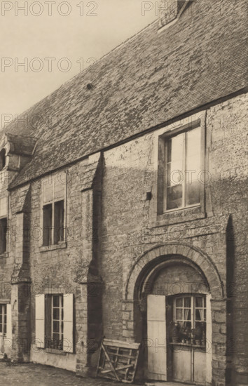 View of the priory in Saint-Gabriel-Brécy, Normandy, Prieuré de Saint-Gabriel, page, photomechanical print, inscription: 'Calvados.', number: 'Pl. No. 25', photographer: Paul Robert, Saint-Gabriel-Brécy, cliché maker: Paul Dujardin, publisher: Lemale & Cie, Le Havre, c. 1890 - in or before 1895, paper, photoaquatint, height 244 mm x width 322 mm, abbey, monastery, convent, Roman Catholic church, A sepia-toned photograph showing a stone building facade with textured roof tiles and rough masonry, featuring multiple rectangular windows with panes and shutters and an arched recessed window with a rounded stone surround, a ladder leaning against the wall near one window, and varied shadows and weathering on the stone surfaces.
