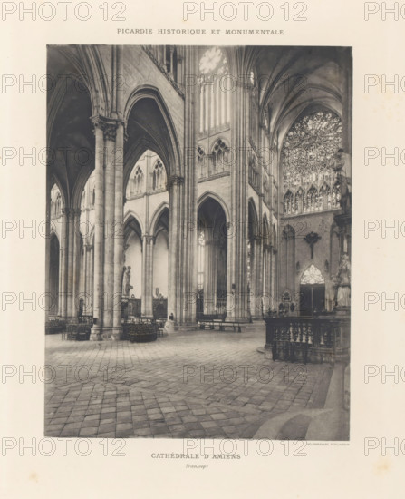 Interior of the transept of Notre-Dame of Amiens, page, photomechanical print, inscription: 'Cathédrale d'Amiens, Portail de la vierge dorée', cliché maker: Paul Dujardin, c. 1888 - in or before 1893, Paul Dujardin, photographer, cliché maker, paper, collotype, photoprint, height 217 mm x width 169 mm, parts of church interior: transept, Amiens, Notre-Dame d'Amiens, A sepia-toned photograph of a cathedral interior showing tall stone columns and pointed arches rising to a vaulted ceiling, a patterned stone floor in the foreground, rows of wooden chairs and benches along the nave, a large ornate rose window with tracery visible high on the right wall, sculpted statues and decorative railings near the sides, and light filtering through tall lancet windows between the columns.