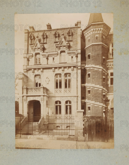 Façade of a building in Paris, photograph, This photo is part of a cover with 35 photos and a title page., number: '1', name: 'De Chiévre. Archte', photographer: Lampué et Cie, Paris, c. 1875 - in or before c. 1880, paper, albumen print, height 226 mm x width 165 mm, façade (of house or building), A sepia-toned photograph of a multi-story building facade showing ornate stonework and a tall brick tower with a conical roof; the left portion of the building features decorative gables, carved stone window surrounds, a small balcony with patterned balustrade, arched entrance framed by columns, and tall windows, while the right side shows a cylindrical brick tower with narrow windows and horizontal stone bands; a metal fence runs across the front with steps leading down to a lower area, and a wooden gate and lamp post are visible near the base of the tower.