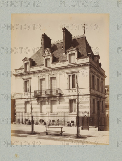 Façade of a villa in Paris, designed by Albert-Ernest Carrier-Belleuse, photograph, This photo is part of a cover with 35 photos and a title page., number: '4', name: 'Carrier Architecte', photographer: Lampué et Cie, Paris, c. 1875 - in or before c. 1880, paper, albumen print, height 220 mm x width 165 mm, detached house in city, façade (of house or building), A sepia-toned photograph of a multi-story European-style house with a steep mansard roof, ornate dormer windows, decorative stonework around the windows and cornice, and tall brick chimneys rising from the roofline. The facade shows shuttered windows, a small wrought-iron balcony above the entrance, and sculpted details beneath the roof edge. In front of the house a metal fence runs along the sidewalk, with two bare young trees protected by circular grates and metal guards. A wooden bench sits on the pavement near the trees and a gated pedestrian entrance is visible to the side. The image has a textured border and shows even lig...