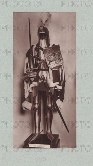 15th-century armor with sword and shield from the army of Charles VII of France, from the collection of the Musée d'Artillerie in Paris, photomechanical print, This print is part of a cover with 36 prints, a title page and a list of images., check stamp: 'PHOTOGLYPTIE, LEMERCIER ET Cie, PARIS', Paris, cliché maker: Lemercier & Cie., c. 1877 - in or before 1882, Lemercier & Cie., photographer, cliché maker, paper, Woodburytype, Woodburytypie, height 275 mm x width 127 mm, hacking and thrusting weapons: sword, armour, protective weapons: shield, A full suit of medieval-style armor displayed on a pedestal, shown front-facing with a closed helmet topped by a large feather plume, a breastplate and articulated arm and leg armor, and gauntleted hands; a long spear is held upright in one hand while a decorated shield with an embossed scene rests against the torso; a fur-trimmed cloak drapes over the shoulders and down the sides, and a sword and scabbard hang at the waist; the armor stands on a...