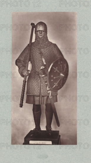 10th-century armor for a cavalryman from the army of Hugo Capet, from the collection of the Musée d'Artillerie in Paris, photomechanical print, This print is part of a cover with 36 prints, a title page and a list of images., check stamp: 'PHOTOGLYPTIE, LEMERCIER ET Cie, PARIS', Paris, cliché maker: Lemercier & Cie., c. 1877 - in or before 1882, Lemercier & Cie., photographer, cliché maker, paper, Woodburytype, Woodburytypie, height 253 mm x width 126 mm, armour, protective weapons: shield, A full-length figure in chainmail armor stands on a raised platform against a plain background, wearing a rounded helmet and a mail coif that covers the neck and shoulders, with a serious facial expression visible through the helmet opening; the figure holds a long pole weapon vertically in the right hand and a round shield with a central boss and decorative rivet patterns in the left arm, while a sheathed sword hangs at the waist and a belt crosses the torso; the armor consists of a mail hauberk ov...