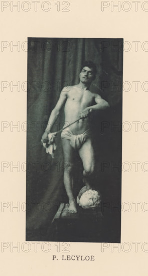 Portrait of an unknown half-naked man, Sentiment d'Art en Photographie, photomechanical print, This print is part of 8 covers with 22 text pages and 89 prints on loose pages in and between the covers., number: 'Vol. 1, No 4, Planche 5.', photographer: P. Lecyloë, cliché maker: anonymous, printer (person): Liorel & Cie., c. 1894 - in or before 1899-01, P. Lecyloë, Liorel & Cie., photographer, cliché maker, printer (person), paper, collotype, photoprint, height 194 mm x width 90 mm, historical persons, man (showing himself) undressed, quasi-nude, A tall rectangular photograph framed by a wide pale border shows a shirtless young man standing on a small platform in front of a dark draped background, wearing a cloth wrapped around his hips and holding a thin rod across his body with one hand while the other hand holds a small bundle of fabric, his gaze directed upward and slightly to one side, one foot planted on the platform and the other foot resting on a sculpted head placed on the platf...