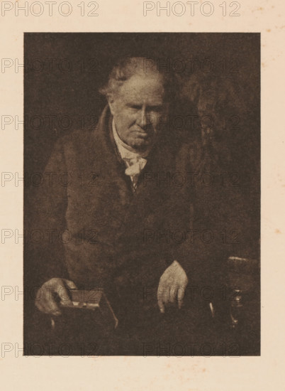 Portrait of Dr. Alexander Monro, page, photomechanical print, photographer: David Octavius Hill, cliché maker: anonymous, c. 1900 - in or before 1905, paper, autotypie, height 151 mm x width 111 mm, Person, Alexander Monro (III), historical persons, A sepia-toned portrait of an older man seated against a dark background, showing his upper body and hands; he wears a dark coat over a lighter shirt with a loosely tied neck cloth, his hair is thinning and receding at the temples, his face is downturned with a somber expression, one hand rests on a small rectangular box held in his lap while the other hand hangs over his knee, and a small jug-like object is visible near his right hand.