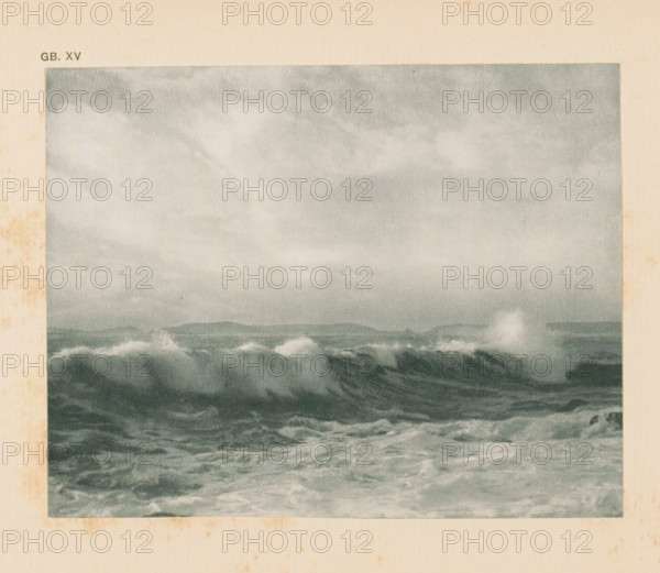 Seascape, page, photomechanical print, inscription: 'GB. XV.', monogram: 'AG', inscription: 'A wind sea by FJ Mortimer', photographer: Francis James Mortimer, cliché maker: anonymous, c. 1900 - in or before 1905, paper, autotypie, height 111 mm x width 141 mm, sea (seascape), A rectangular image shows a grayscale seascape with choppy waves in the foreground and a distant low horizon, topped by a cloudy sky; the surrounding area is a beige paper border with some uneven darker stains along the left and bottom edges.