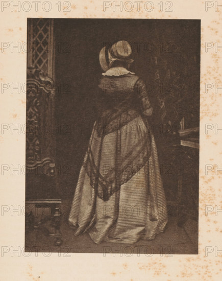 Portrait of Mary Hamilton Ruthven, page, photomechanical print, photographer: David Octavius Hill, cliché maker: anonymous, c. 1900 - in or before 1905, paper, autotypie, height 152 mm x width 112 mm, Person, Mary Hamilton Ruthven, historical persons - BB - woman, A sepia-toned portrait of a woman seen from behind, wearing a floor-length dress with a patterned shawl draped over her shoulders and a small rounded hat; the dress has visible folds and vertical lines, and a ruffled collar is visible at the nape; ornate carved woodwork appears at the left edge and a dark interior fills the background.