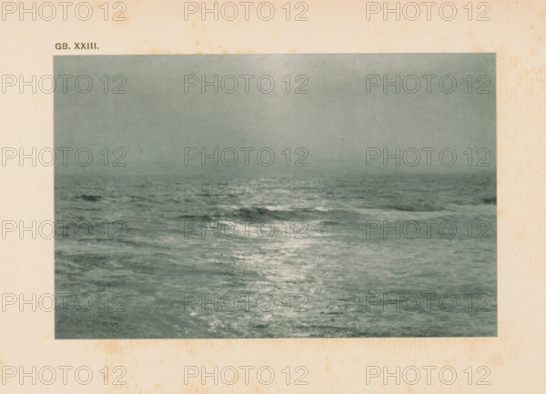 Seascape, page, photomechanical print, inscription: 'GB. XXIII.', inscription: 'Land & sea by WJ Day', photographer: William James Day, cliché maker: anonymous, c. 1900 - in or before 1905, paper, autotypie, height 92 mm x width 143 mm, sea (seascape), A rectangular photograph of a seascape showing a calm, expansive ocean with gentle waves and a reflective sheen on the water surface under a hazy sky, surrounded by a wide off-white paper border with light brown age spots.