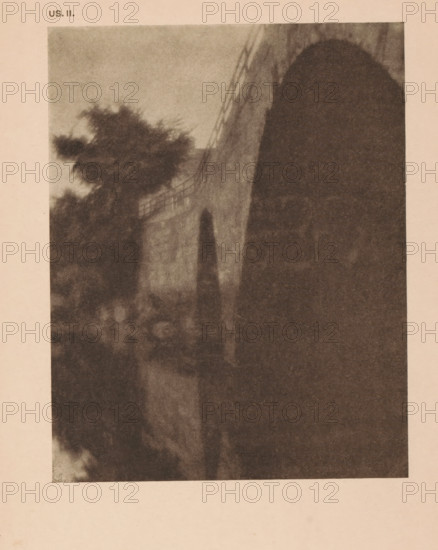 View of a bridge at Ipswich, Massachusetts, page, photomechanical print, inscription: 'US. II.', inscription: 'The bridge Ipswich by Alvin L Coburn', photographer: Alvin Langdon Coburn, Ipswich (Massachusetts), cliché maker: anonymous, c. 1900 - in or before 1905, North America, paper, autotypie, height 145 mm x width 115 mm, bridge in city across river, canal, A grainy sepia-toned photograph showing a large archway on the right with a shadowed interior and a textured wall leading away from it, trees with dark, blurred foliage on the left, a railing or fence running along the top of the wall, and an indistinct foreground of blurred shapes and tones.