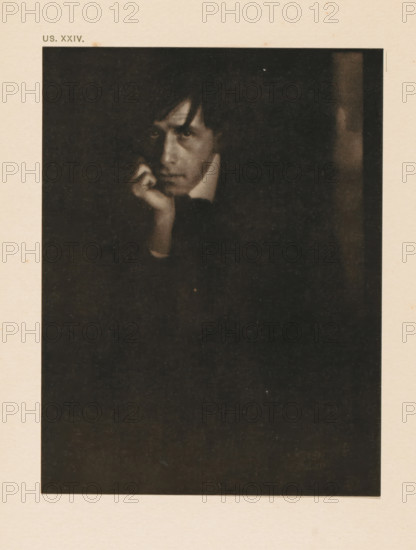Portrait of Clarence Hudson White, page, photomechanical print, inscription: 'Portrait of Clarence H. White by Eduard J. Steichen', inscription: 'US. XXIV.', photographer: Edward Steichen, cliché maker: anonymous, c. 1900 - in or before 1905, paper, two-color autotype, height 149 mm x width 114 mm, Person, Clarence Hudson White, historical persons, portrait, self-portrait of photographer, A dark, grainy portrait of a person with a pale face partially lit against a black background, the person resting their chin on a hand with fingers near the mouth, short dark hair with a fringe falling toward the forehead, a visible high collar and a contemplative facial expression, framed by a wide pale border.