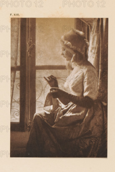Seamstress at the window, page, photomechanical print, inscription: 'At the window by Paul Bergon', inscription: 'F. XIII.', photographer: Paul Bergon, cliché maker: anonymous, c. 1900 - in or before 1905, paper, two-color autotype, height 146 mm x width 102 mm, adult woman, sewing, A sepia-toned image of a seated woman in profile facing a window, wearing a dress with puffed sleeves and a bonnet with ruffled edges, her hands holding a small book or folded object, light falling softly on her face and bodice, a patterned curtain partially visible behind her and ornate window framing with decorative ironwork outside, the lower part of her skirt draped across her lap and the chair.