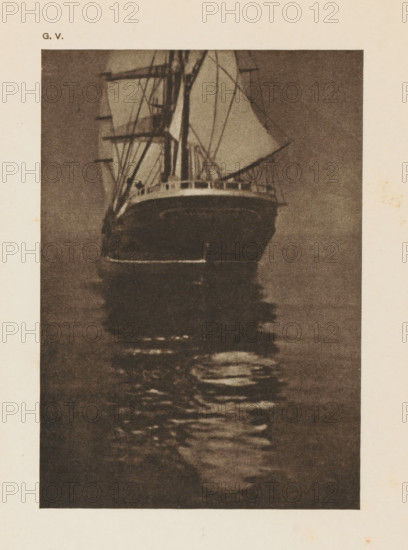 Rear of a sailing ship, page, photomechanical print, inscription: 'A calm sea by O. Hofmeister', inscription: 'GV', photographer: Oskar Hofmeister, cliché maker: anonymous, c. 1900 - in or before 1905, paper, autotypie, height 151 mm x width 106 mm, sailing-ship, sailing-boat, A tall sailing ship seen from the front with masts, spars, and rigging, sails partially furled, a visible deck rail, and the ship’s dark hull reflected in rippling water below, all shown in a grainy, monochrome print on a pale background.