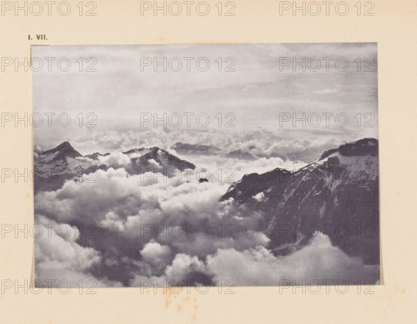 View of the Graian Alps, page, photomechanical print, inscription: 'I. VII.', inscription: 'Clouds Graian Alps by V. Sella', photographer: Vittorio Sella, Graian Alps, cliché maker: anonymous, c. 1900 - in or before 1905, paper, autotypie, height 100 mm x width 143 mm, mountain-range, snow peaks, A sepia-toned photograph mounted on aged paper shows a high-altitude mountain scene with rugged peaks rising above a vast sea of billowing clouds, darker rocky ridges with patches of snow visible near the right edge, softer distant summits partially obscured by mist, and a broad textured sky above the cloud layer.