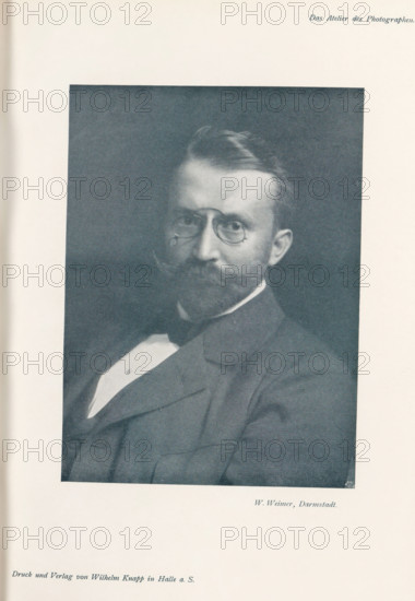 Portrait of an unknown man, page, photomechanical print, inscription: 'Das Atelier des Photographen.', photographer: Wilhelm Weimer, Darmstadt, cliché maker: Meisenbach, Riffarth & Cie., Berlin, printer (person): Wilhelm Knapp, Halle an der Saale, c. 1895 - in or before 1900, printer (person), Hessen, Saxony-Anhalt, paper, autotypie, height 167 mm x width 123 mm, Print on third unnumbered page after page 164., historical persons, A monochrome portrait of a seated man shown from the chest up wearing a dark suit jacket, a white shirt with a visible triangular shirtfront, and a dark bow tie; he has a full mustache and beard, short combed hair, round eyeglasses, and a neutral facial expression, framed by a dark rectangular background centered on a light page.