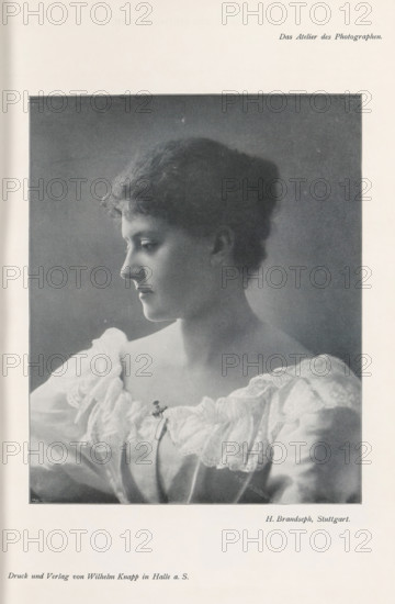 Portrait of an unknown woman, page, photomechanical print, inscription: 'Das Atelier des Photographen.', photographer: Hermann Brandseph, Stuttgart, cliché maker: Meisenbach, Riffarth & Cie., Berlin, printer (person): Wilhelm Knapp, Halle an der Saale, c. 1895 - in or before 1900, printer (person), Baden-Württemberg, Saxony-Anhalt, paper, autotypie, height 173 mm x width 140 mm, Print on third unnumbered page after page 28., historical persons - BB - woman, A black and white portrait of a young woman shown in profile looking left, with short wavy hair and a calm expression, wearing a light-colored dress with a wide lace-trimmed neckline and a small decorative clasp at the center, framed by a dark background and surrounded by a pale border.
