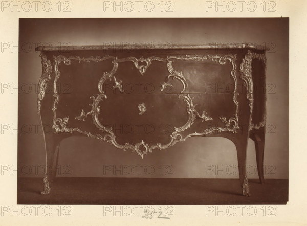 Chest of drawers in the style of Louis XV, from the collection of Christopher Beckett Denison, page, photomechanical print, number: '252', c. 1880 - in or before 1885, paper, Woodburytype, height 123 mm x width 178 mm, ornamental cupboard (wood and other phytogenic material), A photograph of the front and sides of a wooden table with a polished top and ornate carved decorations along its apron and legs, showing curved cabriole legs with carved floral and scroll motifs, a central carved panel with symmetrical scrollwork and foliage designs, decorative edging along the tabletop, and a smooth dark background behind the table.