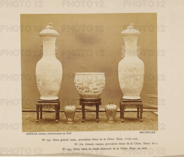 Four Chinese vases and one Chinese kettle, photograph, page, inscription: 'No. 750 Deux grands vases, porcelaine blue de la Chine. Haut 1m60 cent., ', photographer: Ghémar Frères, c. 1870 - in or before 1875, paper, albumen print, height 121 mm x width 140 mm, container of ceramics: jar, jug, pot, vase, kitchen-utensils: cauldron, A sepia-toned photograph shows a symmetrical arrangement of ornamental ceramics on carved wooden stands against a plain backdrop; two tall lidded vases with decorative handles and small sculpted figures on their lids flank a large covered bowl set on a central stand, and two smaller bulbous vases sit on the floor in front of the central piece, all displaying intricate painted patterns and placed on a patterned floor covering.