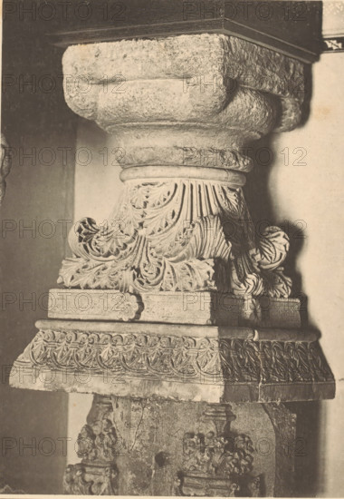 Two shots of capitals with bases in the Paulusabdij in Utrecht, Chapiteaux et bases, XIIe Siècle, page, photomechanical print, monogram: 'JJvY', inscription: 'Chapiteaux et baes, ', inscription: 'LITT. C. - PL. 10', Paulusabdij, cliché maker: Joseph Maes (possibly), Antwerp, after design by Christoffel Plantijn, c. 1875 - in or before 1880, photographer, Utrecht, paper, collotype, photolithography, height 338 mm x width 228 mm, capital (, column, pillar), base (, The image shows a close-up of a carved stone column capital and its base with ornate acanthus leaf and floral motifs, layered moldings, rounded volutes, and textured weathered surfaces, all in a sepia tone against a plain vertical background.