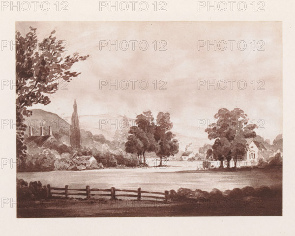 Photo reproduction of a painting depicting a view of Alton Barnes, reproduction, page, photomechanical print, cliché maker: Woodbury Permanent Photographic Printing Company, after painting by Miss Clinton, Alton (Wiltshire), c. 1866 - in or before 1876, photographer, Wiltshire, paper, Woodburytype, height 84 mm x width 114 mm, city-view in general, 'veduta', A sepia-toned landscape showing a wide foreground with a wooden fence along the bottom edge, a body of water or flat field behind it, and clusters of trees of varying shapes and sizes rising toward the middle ground; on the left a tall tree with dense foliage frames the scene, a low roofline and chimneys are partly visible behind shrubbery, and a slender tall tree stands near rolling hills; on the right a small building with arched windows sits among trees, while distant hills and a cloudy sky fill the upper portion of the image.