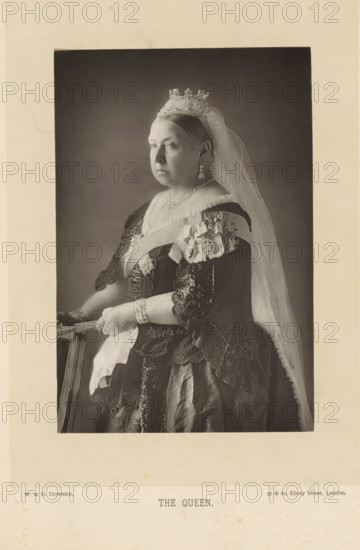 The Queen, Portrait of Victoria of the United Kingdom, page, photomechanical print, inscription: '57 & 61, Elbury Street, London.', photographer: Downey, William & Daniel, London, clichémaker: anonymous, c. 1882 - in or before 1892, paper, Woodburytype, Woodburytypie, height 140 mm x width 93 mm, Person, Victoria (Queen of the United Kingdom and Empress of India), ruler, sovereign - BB - female ruler, A sepia-toned portrait of an older woman shown from the waist up, seated in profile facing left, wearing a light jeweled crown and a long translucent veil that falls over her shoulder; she has a solemn expression and her hair is pulled back, and she is dressed in an ornate dark gown with lace sleeves and layered fabrics, adorned with decorative sashes, a brooch and hanging earrings, and she rests her gloved hands on the back of a chair while wearing bracelets and holding a folded handkerchief.