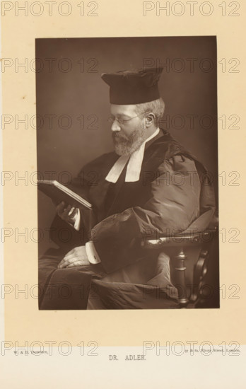 Dr. Adler, Portrait of Hermann Adler, reading a book, page, photomechanical print, inscription: '57 & 61, Elbury Street, London.', photographer: Downey, William & Daniel, London, cliché maker: anonymous, c. 1882 - in or before 1892, paper, Woodburytype, height 139 mm x width 93 mm, Person, Hermann Adler, reading, chief rabbi, A sepia-toned portrait of a bearded man seated in a wooden armchair, wearing dark academic robes with light-colored bands at the collar and a square cap, looking down at an open book held in one hand while the other hand rests on his lap; the image is bordered by a wide pale margin.