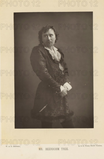 Mr. Beerbohm Tree, Portrait of Herbert Beerbohm Tree, page, photomechanical print, inscription: '57 & 61, Elbury Street, London.', photographer: Downey, William & Daniel, London, cliché maker: anonymous, c. 1882 - in or before 1892, clichémaker, paper, Woodburytype, Woodburytypepie, height 141 mm x width 95 mm, Person, Herbert Beerbohm Tree, portrait of actor, actress, stage costume, A sepia-toned portrait of a man shown from head to mid-thigh against a plain darker background, wearing a patterned dark coat with fur trim at the hem and a light-colored shirt with an open collar, his hair wavy and shoulder-length, a mustache and small goatee on his face, a round medallion suspended on a ribbon at his chest, his hands clasped in front at waist level with visible light-colored cuffs, a slender object tucked at his side, and a neutral expression with his gaze directed slightly to one side.