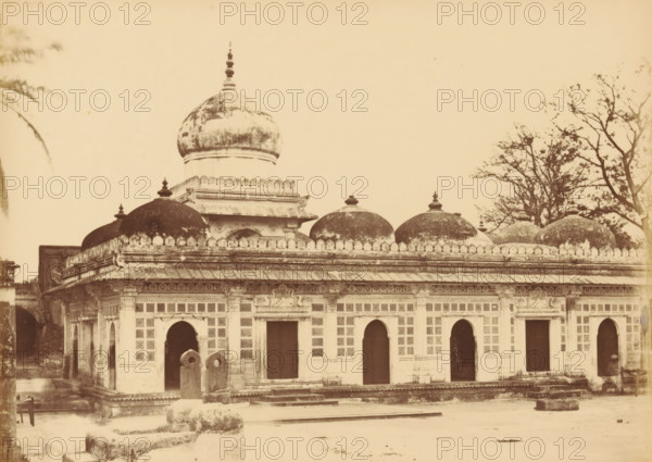 Shah Wuze-U-Deen's Tomb, View of a Shah's tomb in Ahmedabad, photograph, page, number: '116.', photographer: Thomas Biggs, Ahmedabad (city), c. 1856 - in or before 1866, Gujarat, paper, albumen print, height 135 mm x width 189 mm, grave, tomb, A sepia-toned photograph of a building with a row of arched doorways along its façade and decorative latticework panels above and between the arches, a low parapet capped with small scalloped ornamentation, and a series of domes rising above the roofline including a larger central dome with a finial and several smaller rounded domes with finials; the building shows weathering and darkened patches on the domes and upper surfaces, carved cornices and ornamental friezes under the roof, and a set of stone structures and steps in the foreground, with bare-branched trees visible to the right and a partial palm frond at the left edge.