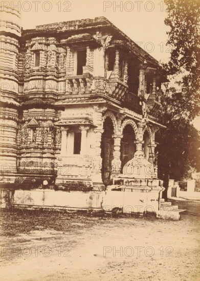 View of the Hutheesing Temple in Ahmedabad, Shet Huttising's Temple.- The Porch, photograph, page, number: '119.', photographer: Thomas Biggs, Ahmedabad (city), c. 1856 - in or before 1866, Thomas Biggs, photographer, Gujarat, paper, albumen print, height 197 mm x width 144 mm, places and objects of worship, Hinduism, Buddhism, Jainism, Hutheesing temple, A sepia-toned photograph of a carved stone building façade with ornate columns, balustrades, and arched openings, showing layered horizontal bands of decorative relief and sculpted figures on the walls; a small dome-like stone structure sits on a raised platform near the entrance steps, and trees are visible to the right, with a textured ground area in the foreground.