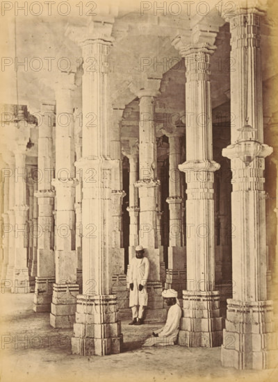 Interior of the Jama Masjid in Ahmedabad, The Jumma Mosque.- Pillars in the Interior, photograph, page, number: '18.', inscription: 'F2', photographer: Thomas Biggs, Ahmedabad (city), c. 1856 - in or before 1866, Gujarat, paper, albumen print, height 201 mm x width 148 mm, temple, shrine, Islam, Mohammedanism, column, pillar, architecture, Jama Masjid (Ahmedabad), A sepia-toned photograph showing a large interior space filled with tall carved stone pillars arranged in rows, each pillar featuring fluted shafts and ornate capitals and bases with layered stonework; two men in traditional light-colored clothing and turbans are among the pillars, one standing and leaning against a pillar and the other seated on the floor near a base; the floor appears smooth and worn, the ceiling is supported by the pillars with visible stone beams, and a hanging lantern is suspended from one pillar.