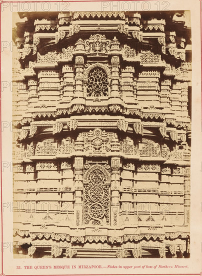 Decoration on the base of a minaret of the Rani Rupamati Mosque in Ahmedabad, The Queen's Mosque in Mirzapoor.- Niches in upper part of base of Northern Minaret, photograph, page, number: '33.', inscription: 'K', photographer: Thomas Biggs, Ahmedabad (city), c. 1856 - in or before 1866, Thomas Biggs, photographer, Gujarat, paper, albumen print, height 188 mm x width 136 mm, temple, shrine, Islam, Mohammedanism, base (, column, pillar), ornamenting, decorating, applied arts, Rani Rupamati Mosque, A close view of an ornate stone façade with layered horizontal bands and carved decorative trim, featuring an arched central niche with an intricate lattice pattern, flanked by carved pilasters and small domed motifs, repeated ornamental brackets and scalloped edges along projecting ledges, and repeated geometric and floral relief panels across the surface.