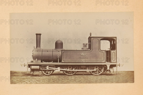 Steam locomotive for passenger transport made by Sharp, Stewart and Company, photograph, page, number: '774', inscription: 'Class 774. Passenger tank engine', c. 1874 - in or before 1884, photographer, paper, albumen print, height 83 mm x width 143 mm, steam locomotive, A sepia-toned photograph of a steam locomotive shown in profile on a cobblestone surface, with a tall cylindrical smokestack at the front, a rounded dome behind it, a rectangular cab with an open cab doorway and an arched window cutout, and a tank-like side panel with decorative border molding; visible running gear includes large spoked driving wheels, connecting rods, springs, and buffers with chain links at both ends, and small external fittings and pipes along the boiler and side tank.