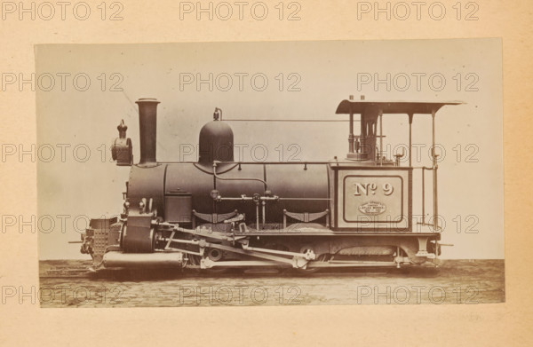 Steam locomotive made by Sharp, Stewart and Company, photograph, page, number: '810', inscription: 'Class 810. Tank engine, for light 2ft. Oin. Gauge Railways.', c. 1874 - in or before 1884, photographer, paper, albumen print, height 83 mm x width 144 mm, steam locomotive, A sepia-toned photograph shows a side view of a steam locomotive mounted on a light background with a textured border, featuring a cylindrical boiler, a tall smokestack near the front, a rounded dome toward the middle, and an open cab area at the rear with a roof supported by slender posts. The front of the locomotive displays a boxy assembly with riveted plates and a small lantern mounted near the smokestack, while the running gear below includes visible pistons, connecting rods, springs, and wheel components. Pipes and handrails run along the side of the boiler, and a rectangular panel is set into the rear side of the locomotive. The ground beneath the locomotive shows cobblestone paving.