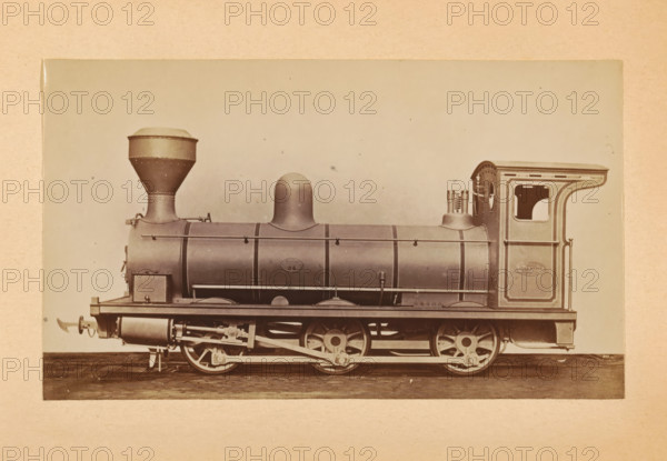 Goods steam locomotive made by Sharp, Stewart and Company, photograph, page, inscription: 'Class 677. Goods engine.', number: '677', c. 1874 - in or before 1884, photographer, paper, albumen print, height 83 mm x width 141 mm, steam locomotive, A sepia-toned photograph of a steam locomotive shown in profile, with a rounded dome on the boiler and a tall, flared smokestack toward the front, mounted on a frame with visible driving wheels and connecting rods; the cylindrical boiler has horizontal bands and handrails, and a rectangular cab at the rear with a curved roof and an open window; beneath the boiler there are cylinders and mechanical linkages, and the whole engine sits on a flat surface against a plain, light background.