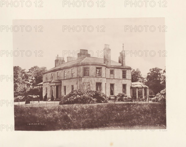 Ibroxhill, photograph, page, photographer: Thomas Annan, Glasgow, c. 1868 - in or before 1878, paper, carbon print, height 115 mm x width 160 mm, rural housing, eg country-house, villa, cottage, façade (or house or building), A sepia-toned photograph of a large two-story stone house with a curved central bay and multiple tall chimneys rising from a hipped roof, tall sash windows on both floors, a columned entrance with a small pediment, a conservatory-like glass extension to one side, shrubs and flowering bushes in front of the building, a low fence along the front perimeter, a stretch of grass in the foreground, and trees partially visible behind and to the sides of the house.