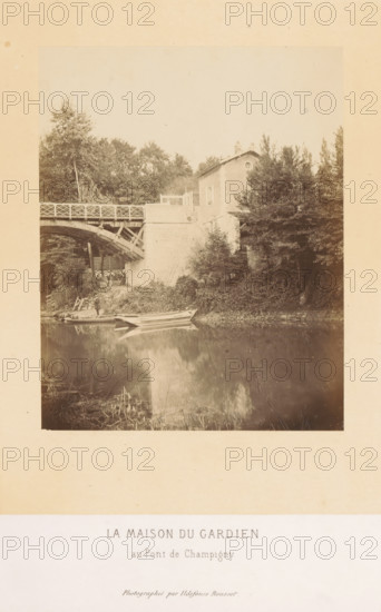 Bridge keeper's house of the Pont de Champigny in Champigny-sur-Marne, La maison du gardien au Pont de Champigny, photograph, page, photographer: Ildefonse Rousset, Île-de-France, c. 1860 - in or before 1865, Ildefonse Rousset, photographer, paper, albumen print, height 152 mm x width 122 mm, river, bridge, housing, Marne (river), Pont de Champigny, Champigny-sur-Marne, A sepia-toned photograph shows a riverbank scene with a wooden arched bridge spanning from the left toward a stone embankment, a small house partially hidden by trees perched above the embankment, dense foliage and trees surrounding the house and bridge, a narrow boat moored at the water’s edge near a small grassy and rocky slope, the water reflecting the boat, embankment, and nearby vegetation, and a wide pale margin around the photograph with a printed caption area beneath the image.