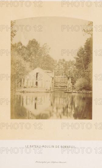Ship mill at Bonneuil-sur-Marne, Le bateau-moulin de Bonneuil, photograph, page, photographer: Ildefonse Rousset, Bonneuil-sur-Marne, c. 1860 - in or before 1865, paper, albumen print, height 152 mm x width 122 mm, river, watermill in landscape, Marne (river), A faded sepia photograph showing a riverside scene with a wooden building and adjoining waterwheel structure partially obscured by surrounding trees, the building reflected in the calm water in front, trees and foliage filling the background and framing the scene, all set within a pale mount.