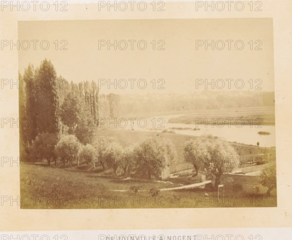 The Joinville a Nogent, View of the Marne near Joinville, photograph, page, photographer: Ildefonse Rousset, Île-de-France, c. 1860 - in or before 1865, paper, albumen print, height 130 mm x width 175 mm, river, Marne (river), A sepia-toned landscape photograph showing a river winding through flat land with grassy banks and small islands, a line of tall trees along the left bank and more scattered trees and shrubs in the foreground, a fenced garden area and a low stone wall near the lower right, and a small solitary figure standing on the riverbank toward the right side of the scene.