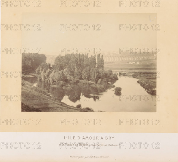 View of the Île d'Amour at Bry-sur-Marne, L'Ile d'Amour a Bry, photograph, page, photographer: Ildefonse Rousset, Île-de-France, c. 1860 - in or before 1865, Ildefonse Rousset, photographer, paper, albumen print, height 115 mm x width 155 mm, island, city-view in general, 'veduta', river, Marne (river), Bry-sur-Marne, Île d'Amour, A sepia-toned photograph mounted on a beige matte shows a river with reflective water bordered by grassy banks and a cluster of trees, some tall and narrow and others fuller, forming an island-like grouping; the water reflects the trees and sky, and a distant arched viaduct spans the background across the landscape with open fields and a few small buildings nearby, all framed by the matte with a large blank area below the image.