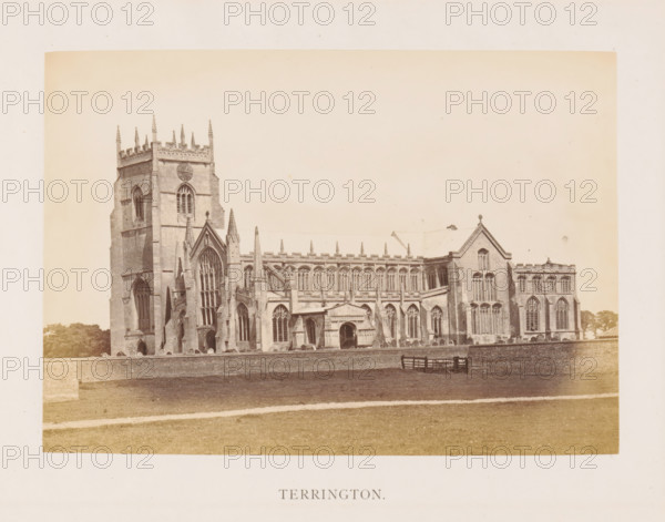 Terrington, photograph, page, photographer: Edward Johnson, Terrington Saint Clement, c. 1858 - in or before 1869, Norfolk (county), paper, albumen print, height 124 mm x width 178 mm, church (exterior), facade (of house or building), Saint Clement's Church (Terrington Saint Clement), A wide exterior view of a large stone church building with Gothic architectural features including tall arched windows, ornate tracery, buttresses, pinnacles, and a square tower with decorative battlements and slender spires; the church sits behind a low brick wall with a grassy foreground and a simple wooden bench near the wall, and trees are visible at the edges of the scene.