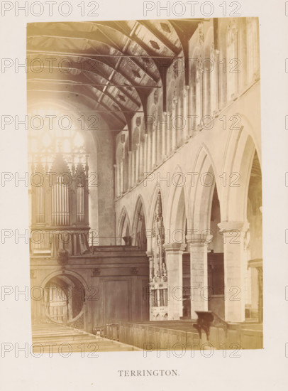 Terrington, photograph, page, photographer: Edward Johnson, Saint Clement's Church (Terrington Saint Clement), c. 1858 - in or before 1869, Edward Johnson, photographer, Norfolk (county), Terrington Saint Clement, paper, albumen print, height 177 mm x width 125 mm, interior of church, parts of church interior: aisle, A sepia-toned interior photograph showing a vaulted ceiling with exposed wooden beams and a series of tall arched openings along the right wall supported by stone columns with carved capitals. To the left a large ornate organ case with vertical pipes sits above wooden paneling and a circular doorway opening beneath. Wooden pews run along the nave in the foreground, and decorative stone tracery and carved details are visible between the arches and near the windows, with bright light filtering through a large window at the far end.